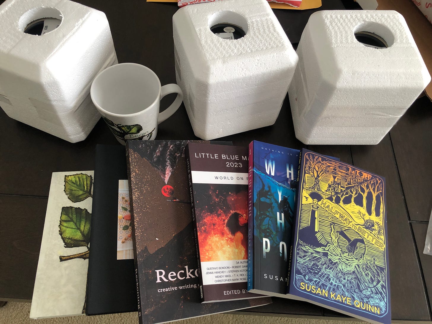 display of all the August giveaway items: anthologies, notebooks, mugs