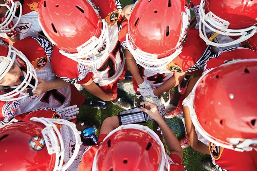 An aerial view of youth football players huddled in red helmets