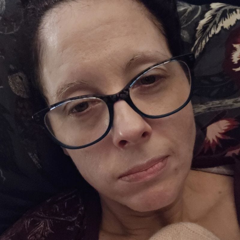 A woman with glasses on in bed feeling ill