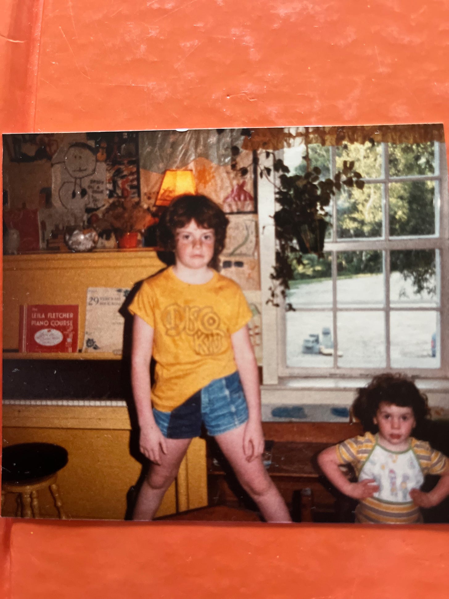 Photograph of two children one standing on a wooden box wearing a "Disco Kid" t-shirt, the other below with curly hair.