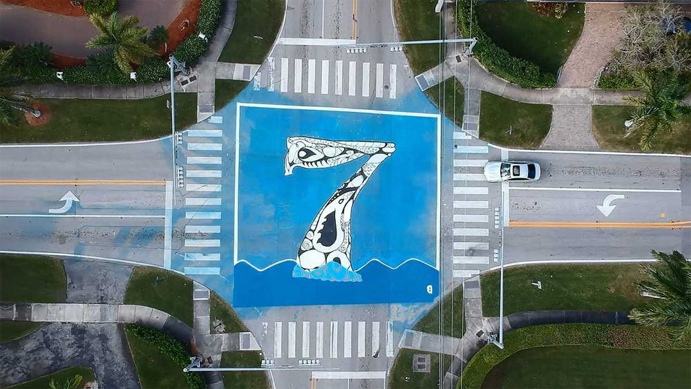 Aerial photograph from about 50 feet up, looking straight down on an intersection in which a huge stylized numeral 7 is painted on a blue background