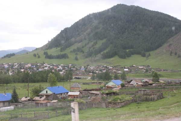 A small town with houses and metal roofs in front of a high mountain