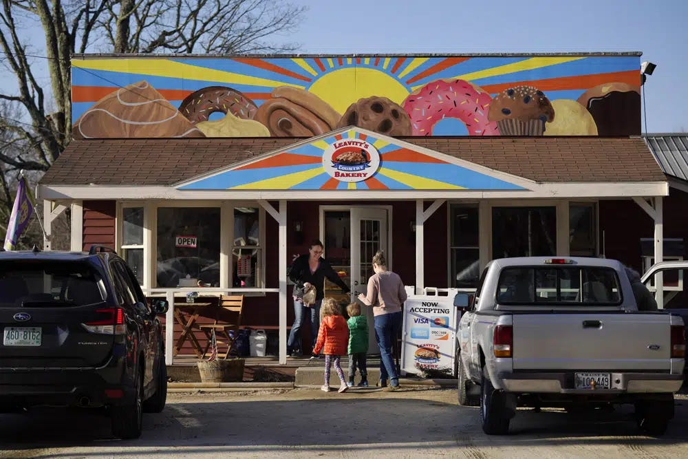 A customer holds the door for a family arriving at Leavitt's Country Bakery, Thursday, April 13, 2023, in Conway, N.H. The large painting of pastries created by students and displayed over the bakery is at the center of a legal battle pitting a zoning ordinance against freedom-of-speech rights. (AP Photo/Robert F. Bukaty)