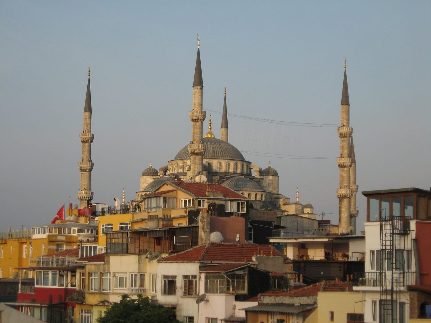 The Blue Mosque in Istanbul, with various buildings in the foreground, under an early morning clear sky