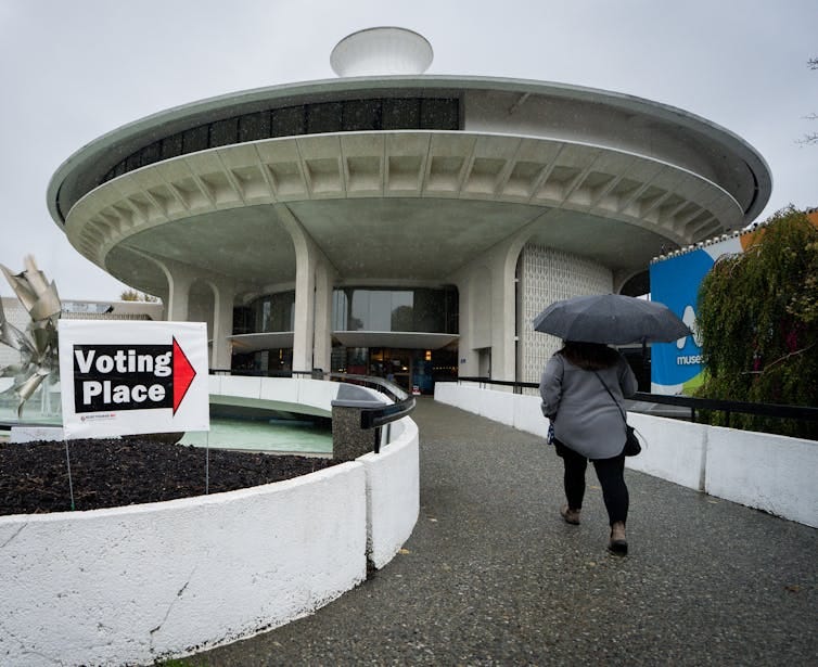 A voter carrying an umbrella walks into an urban polling station.