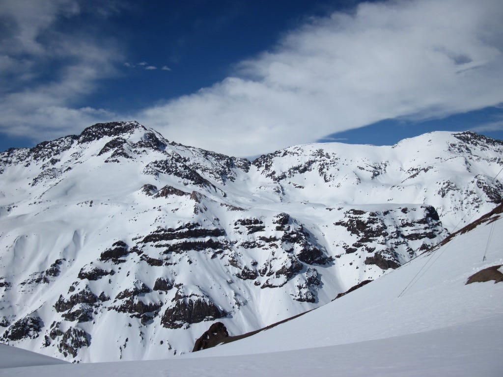 mountain range covered in snow with blue sky and clouds above mountain range covered in snow with blue sky and clouds above