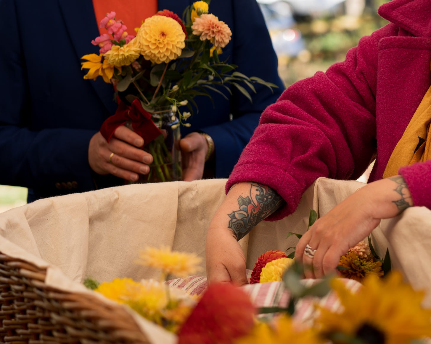 Open willow coffin being filled with garden flowers by friends. Tattoos on show.