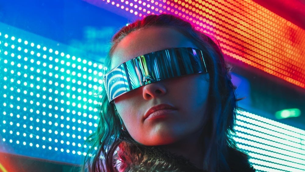 Woman wearing shades standing in front of a bright neon backdrop