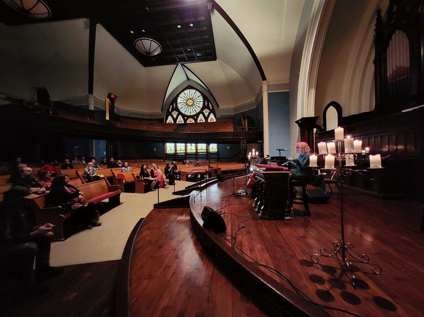 Elle sitting behind pulpit (side view) with audience in church pews and stained glass window 