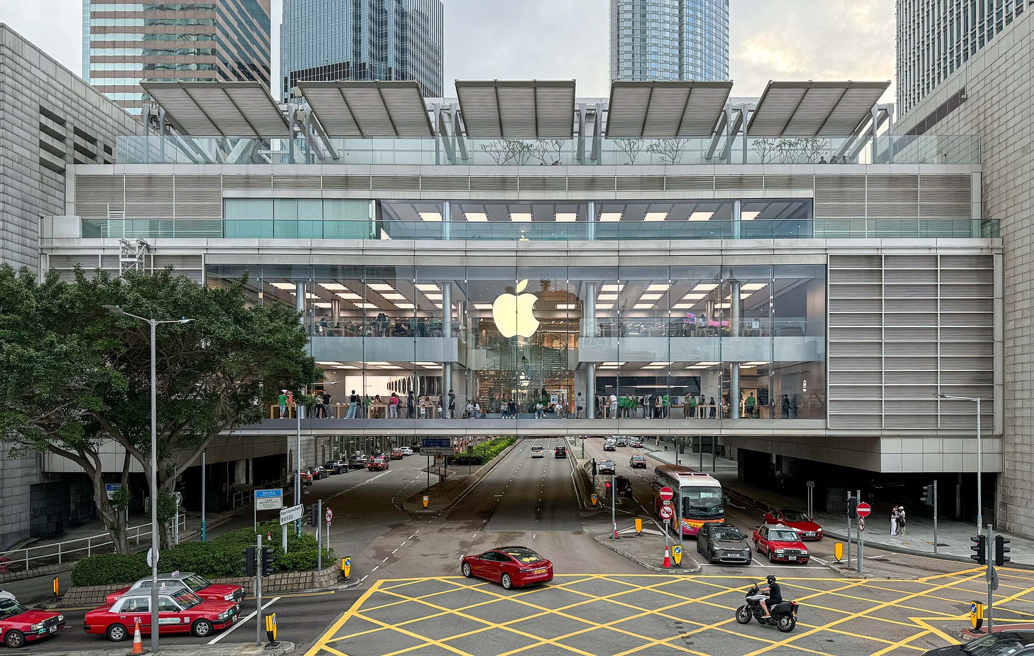 Apple ifc mall, pictured from the store's exterior. Cars and pedestrians cross the busy intersection below. Inside the store, an Apple Pickup counter has been added to the lowest level.
