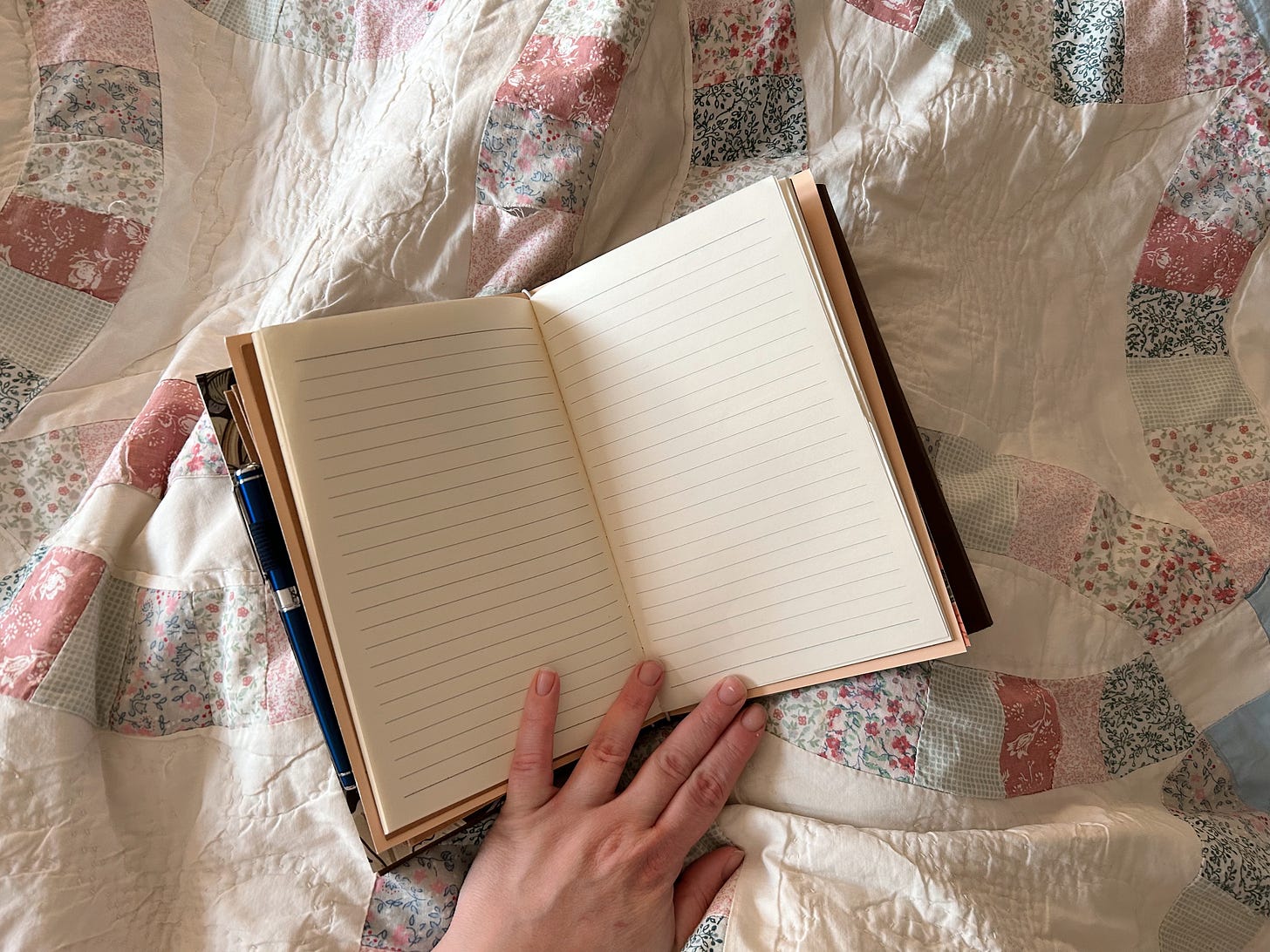 A pale hand holds open a lined traveler's notebook on a handmade quilt of pink and blue interlocking rings