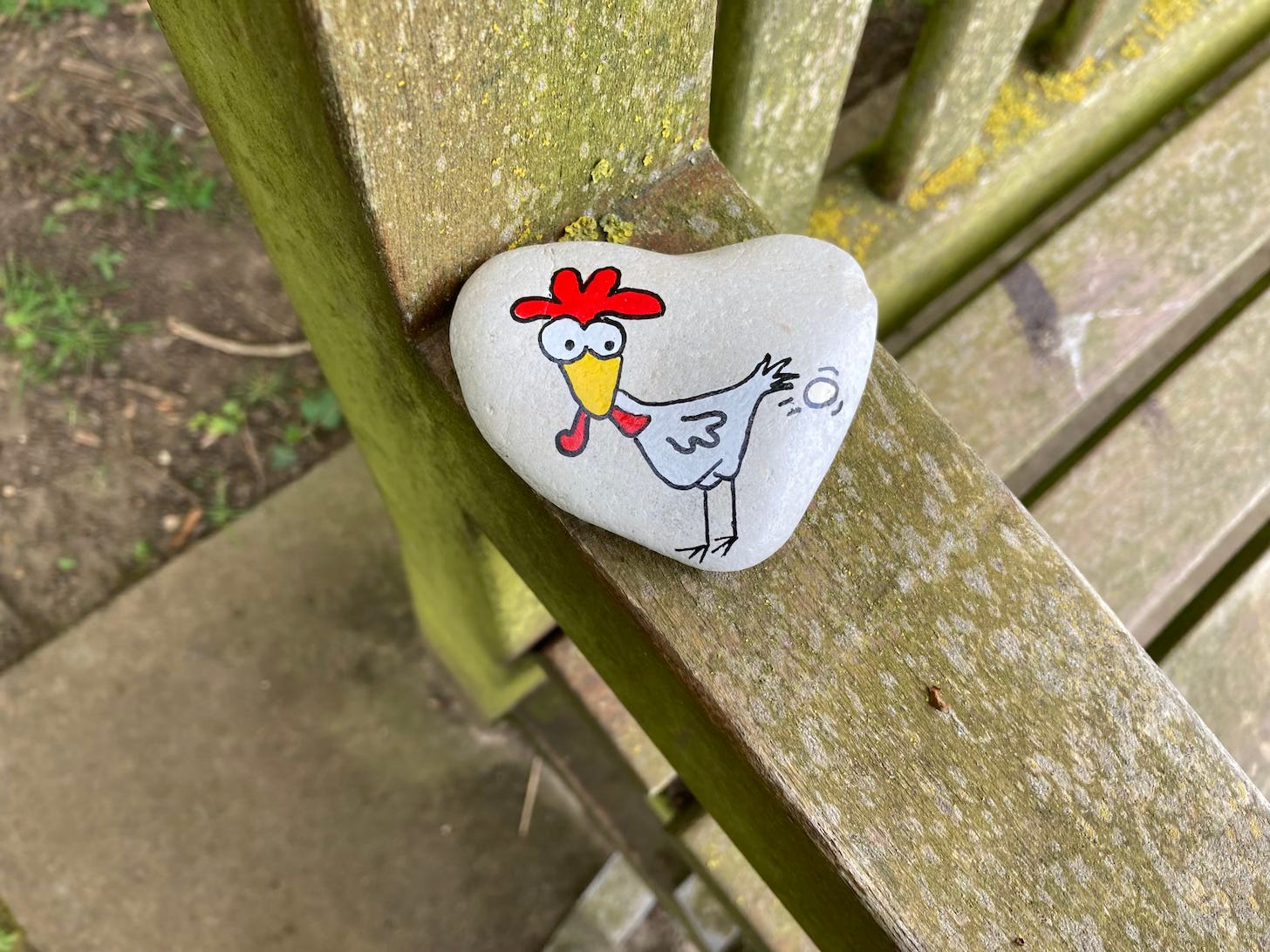 Heart shaped stone painted with chicken laying an egg in comical fashion