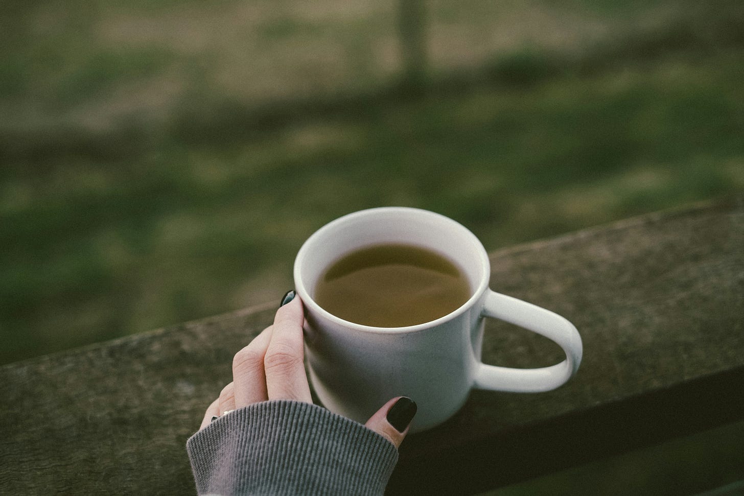 Hand resting mug of green tea on a balcony