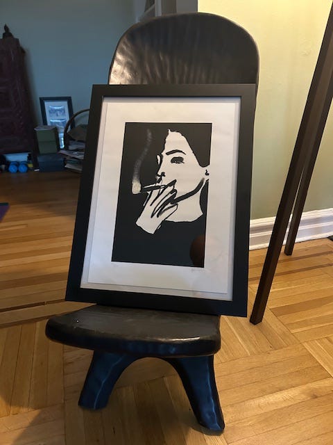 A framed drawing of a woman smoking a cigarette rests on a chair.