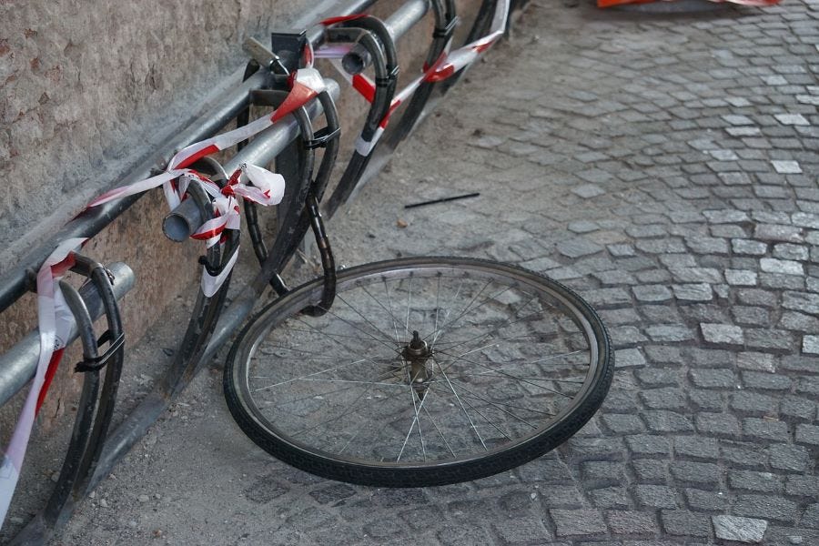 A bike rack attached to a brick wall, with a bicycle wheel fastened to the bike rack with a chain lock.