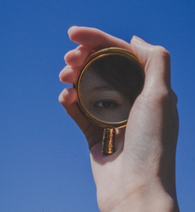 Woman's eye seen in reflection of gold hand-held mirror, against blue sky