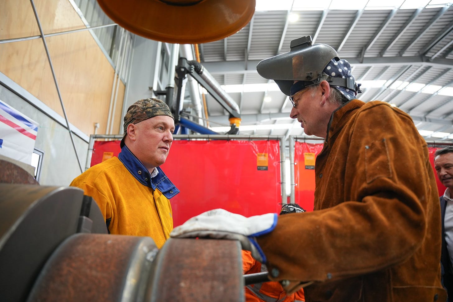 Image of Christopher Luxon visiting a factory with a backward baseball cap.