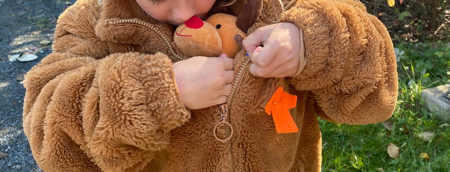 A child tucking a stuffed reindeer into the front of her brown coat. There's an orange shirt pinned to the front of the coat