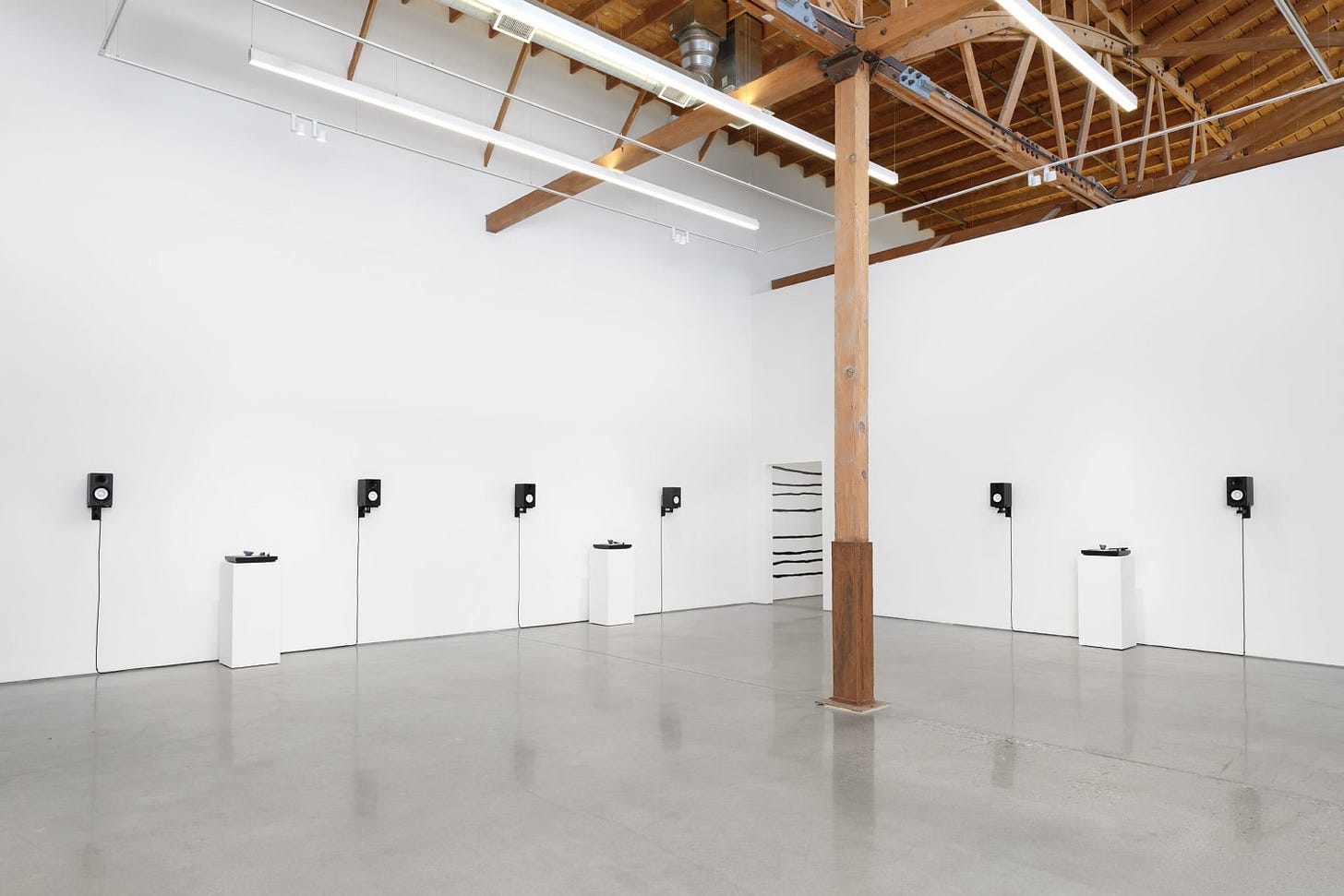 An art installation in a large white wall gallery includes studio monitor speakers mounted to the wall in pairs with a vinyl turntable in between each.