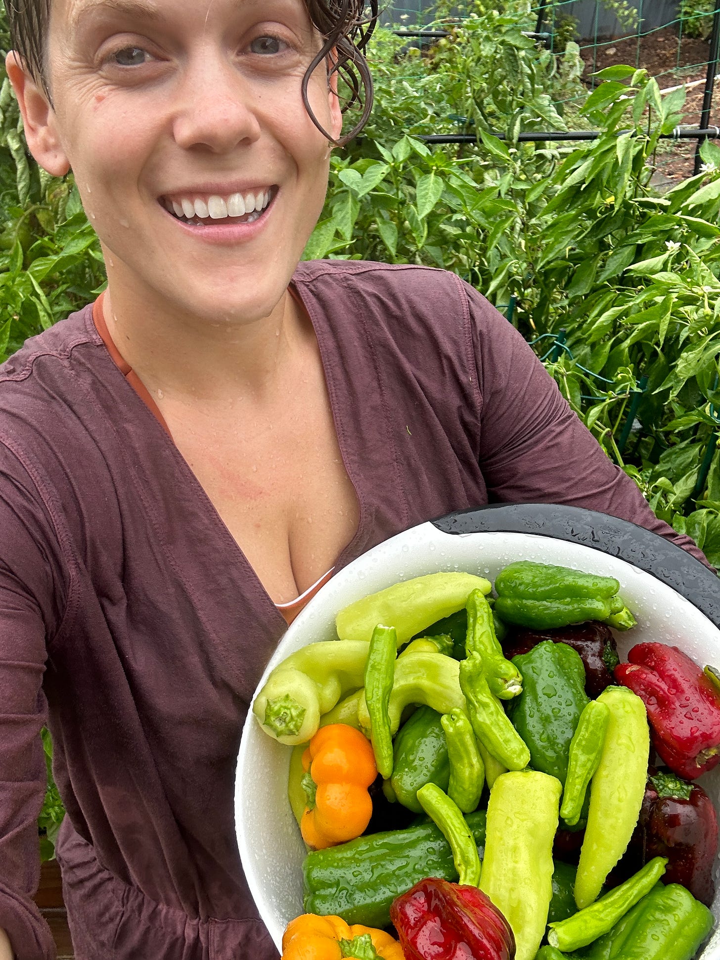 girl smiling in the rain holding a basket of green, orange, and red peppers