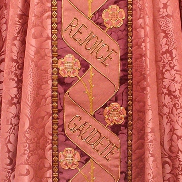 A piece of heavy pink floral material hands down. It features text reading "Rejoice Gaudete"