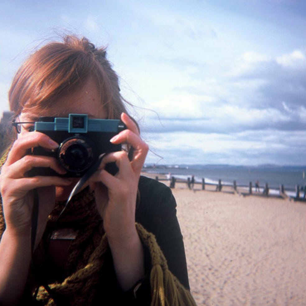 Lizzy on a beach holding a camera over her face
