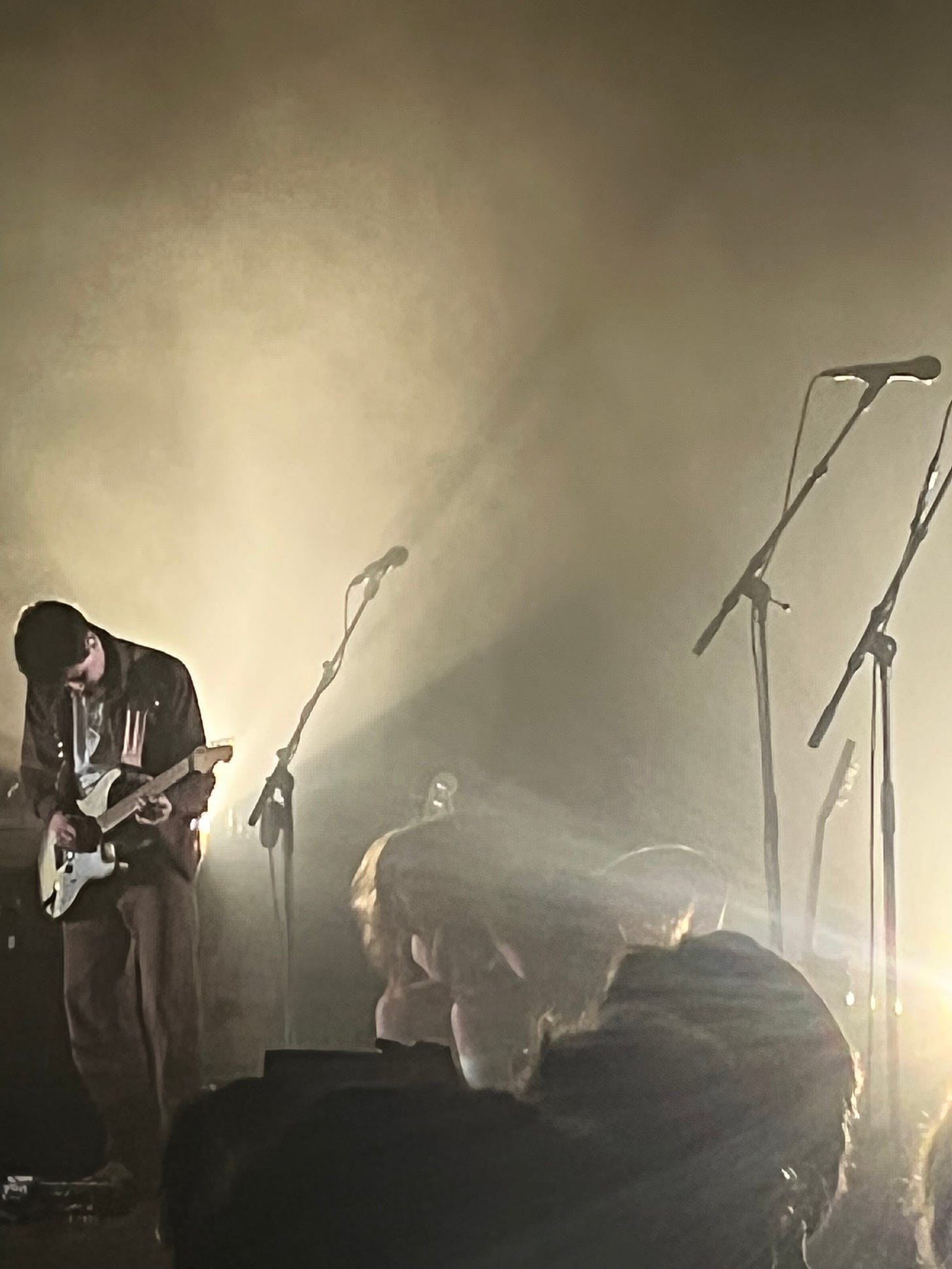 three microphones, one bas player and one sitting human surrounded by fog and murky light