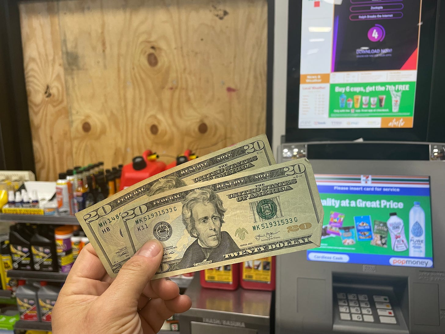Two $20 bills in front of an ATM in front of a boarded-up window