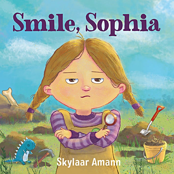 Cover of Smile, Sophia, which includes Sophia scowling with her arms crossed. There is a shovel, pail, pick ax, and dinosaur plushie in the background, which is a lawn full of holes Sophia dug. There's also a big bone sticking out of a pile of dirt.