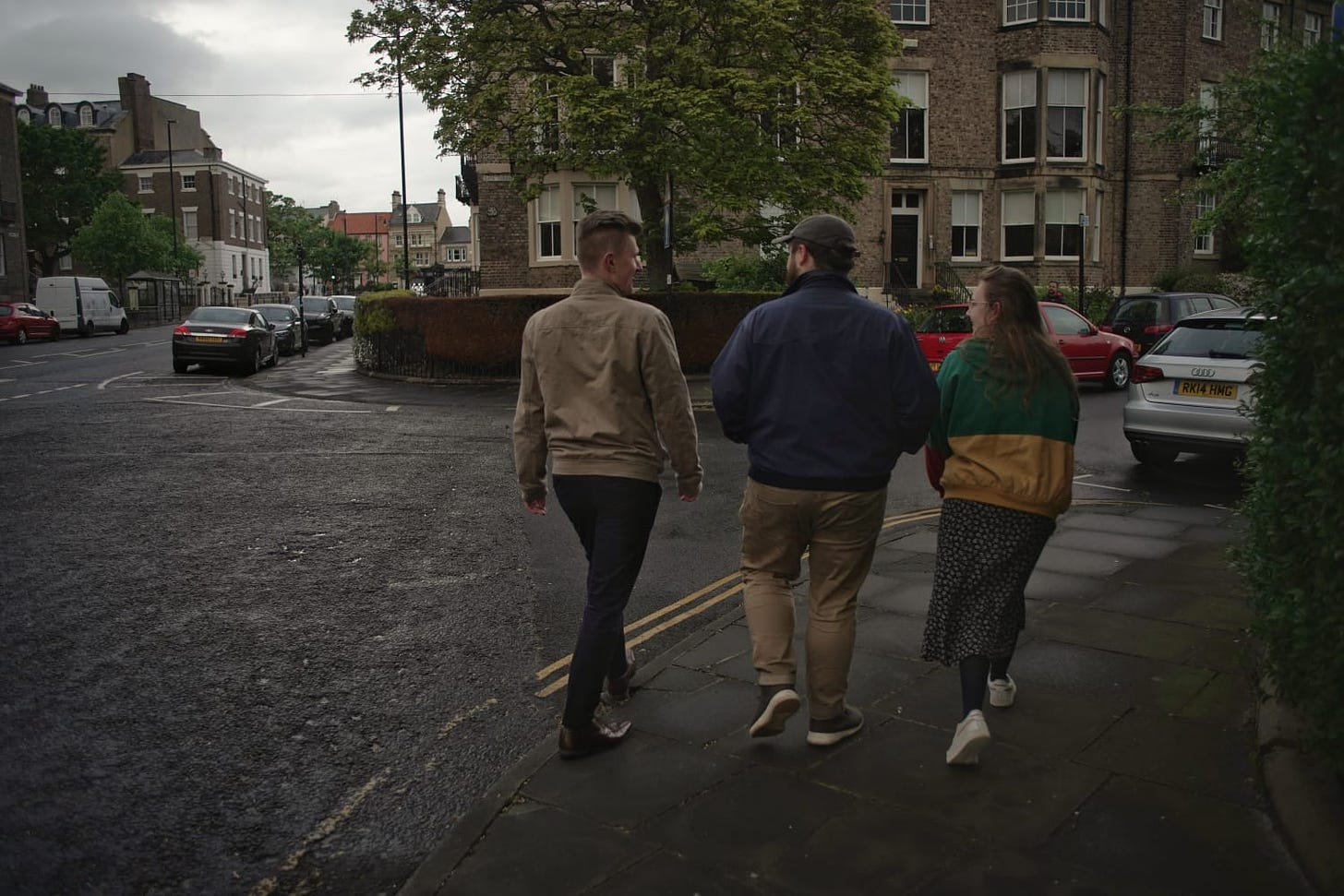 The EXIT Press team in 2022. On the left is Christian, a white man with dirty blonde/brown hair, in a tan jacket. In the middle is Kieran, a white non-binary person wearing a cap and a blue jacket. On the end is Eve, a white woman with brown hair wearing a green and yellow jacket. They are walking around the corner of a road together. The vibe is that we're walking away to something else. Taking the EXIT, perhaps.