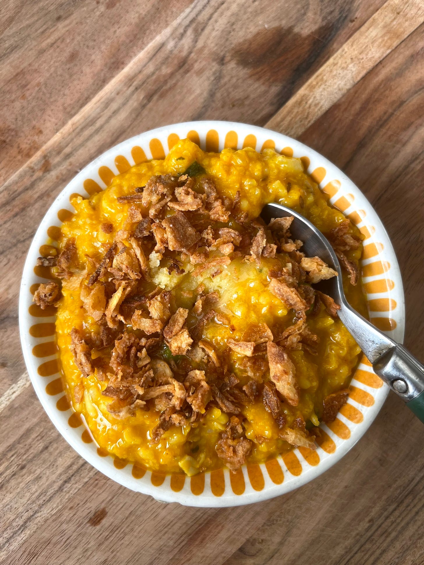 rice porridge in a bowl topped with crispy fried onions and ghee and spoon on top