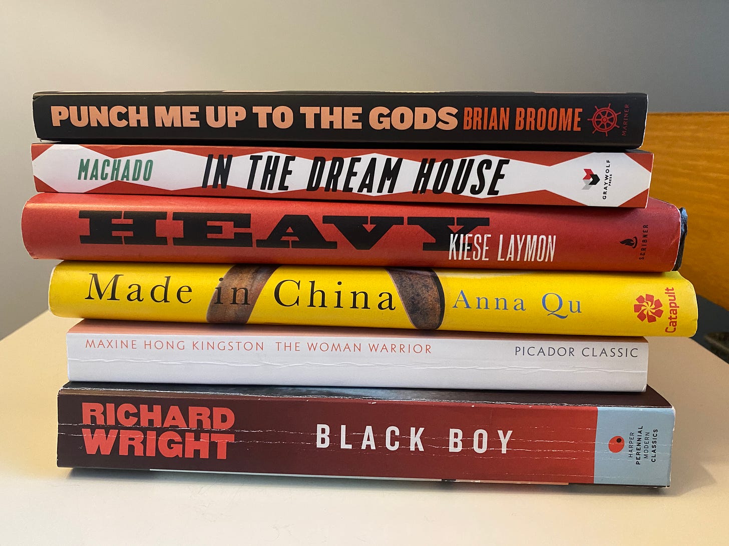 Books stacked sideways include: Richard Wright, Black Boy, Maxine Hong Kingston, The Woman Warrior, Anna Qu, Made in China, Kiese Laymon, Heavy, Carmen Machado, In the Dream House, Brian Broome, Punch Me Up to the Gods