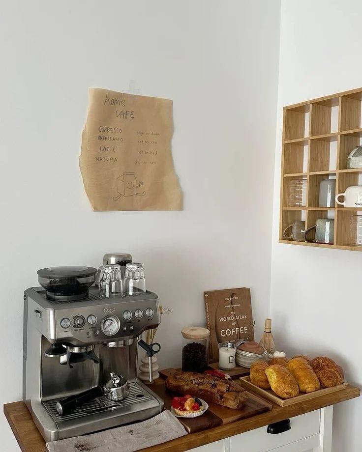 This may contain: a coffee maker sitting on top of a wooden counter next to some pastries and drinks