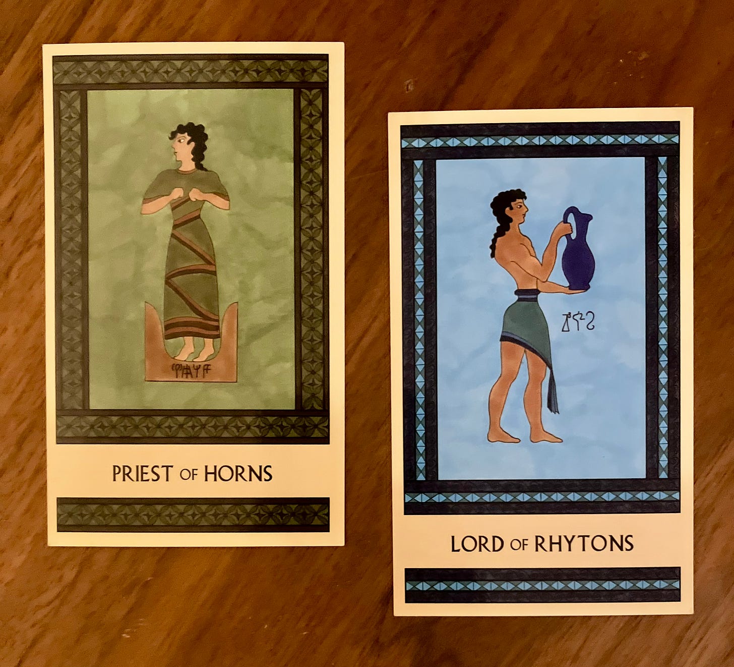 Two Minoan Tarot cards side by side on a brown wood surface. The Priest of Rhytons is painted in shades of green and brown. It shows a Minoan man in a long robe, standing on a pair of sacred horns, facing left. The Lord of Rhytons is painted in shades of blue. It shows a Minoan man standing, facing right, wearing a knee-length kilt. He holds up a large blue pitcher in front of himself. 