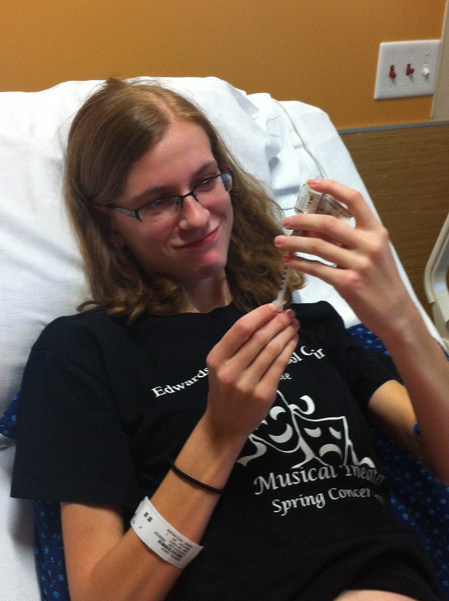 Young, thin girl in hospital bed, drawing insulin from bottle with syringe.