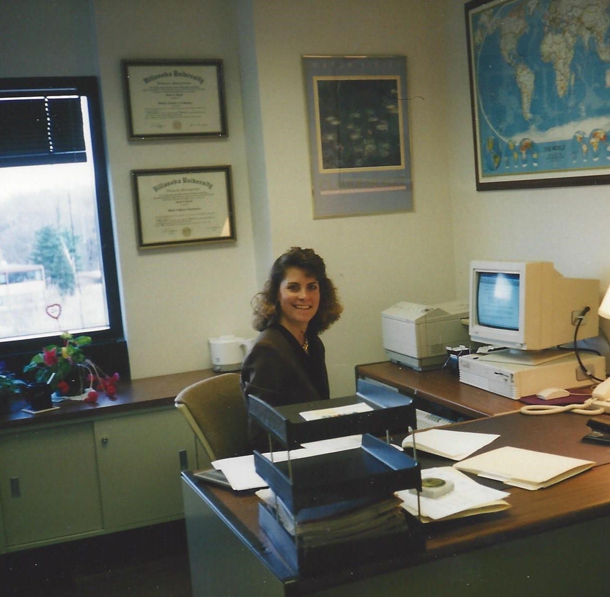 20-something woman seated behind a desk in an office of her very own