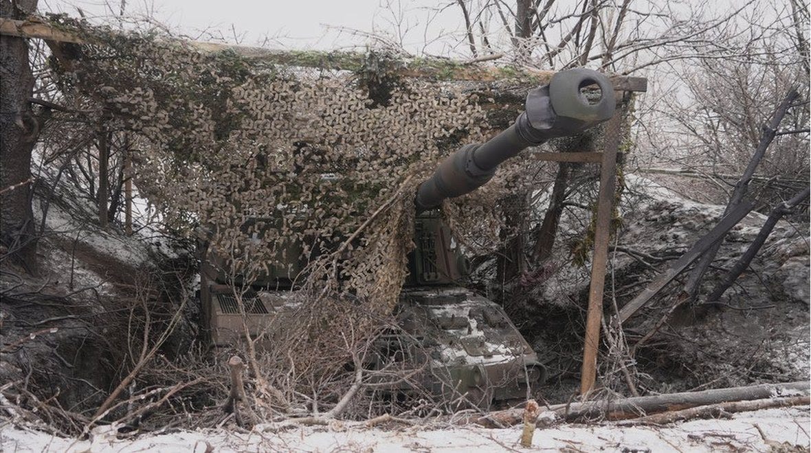 A tank stands in the snow partially covered by a military tent