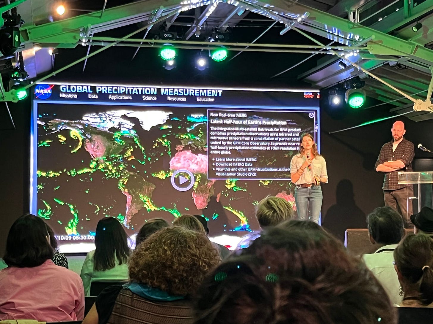 Bild von der Konferenz in Lissabon zu Klimajournalismus. Zu sehen ist eine Frau, die auf dem Podium die Karte zu Regendaten der NASA erklärt. Das Foto wurde aus dem Publikum aufgenommen.