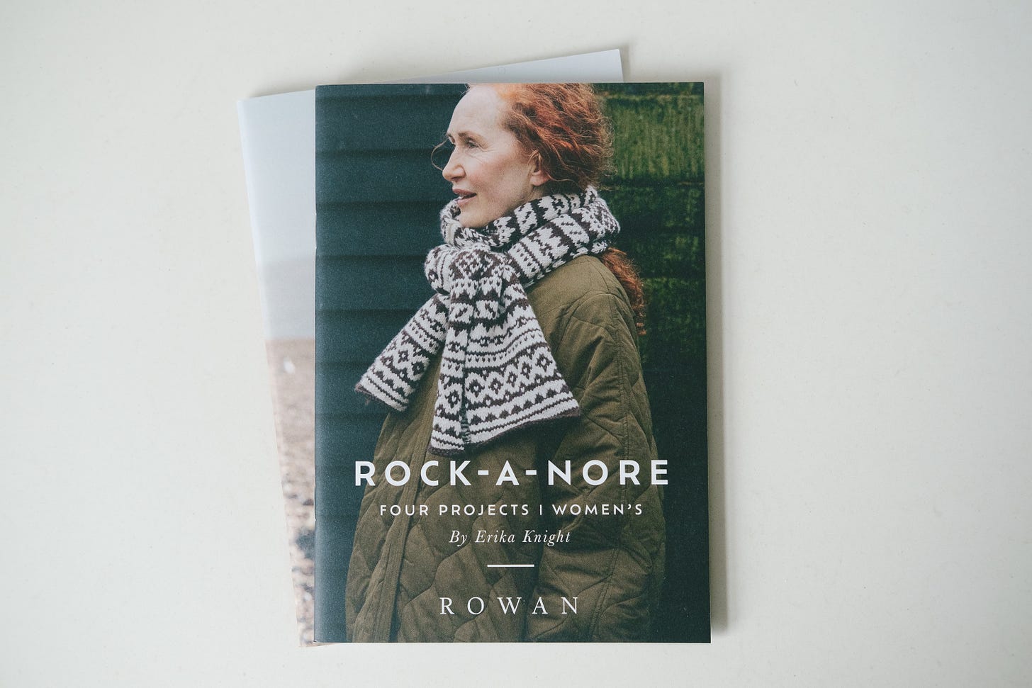 A top-down image of 2 books; Rock-a-Nore and Saltwashed by Erika Knight. On the cover is a woman in a padded coat and striped patterned wool scarf.