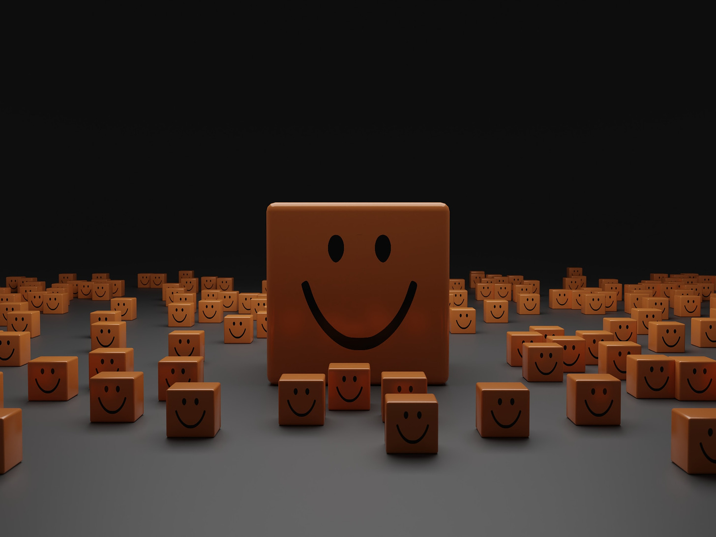 Sfondo nero e superficie orizzontale grigia su cui poggiano sparsi tanti cubi arancio con la faccia rivolta verso chi guarda che rappresenta una bocca sorridente e due occhi. Al centro c'è uno di questi blocchi grande quattro volte gli altri.