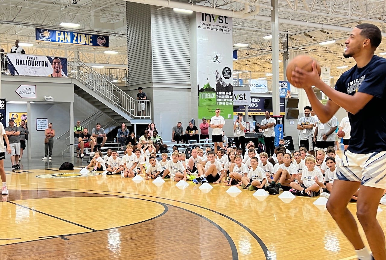 Wearing a navy basketball camp t-shirt, Pacers guard Tyrese Haliburton shoots a 3-pointer in front of kids at his camp.