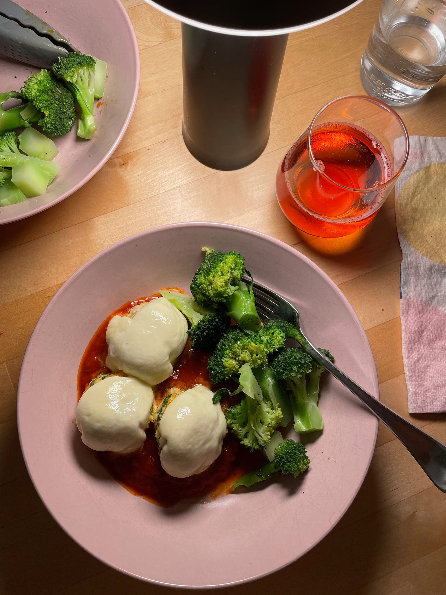 Three chicken meatballs in a bowl topped with melted mozzarella, in a bowl with tomato sauce and steamed broccoli.