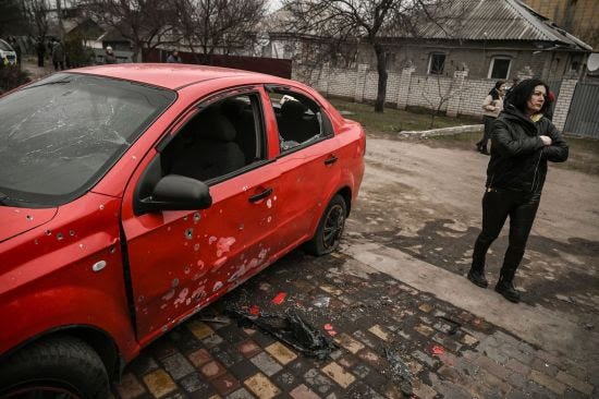 A woman stands next to a damaged car by cluster bombs in Ukraine.