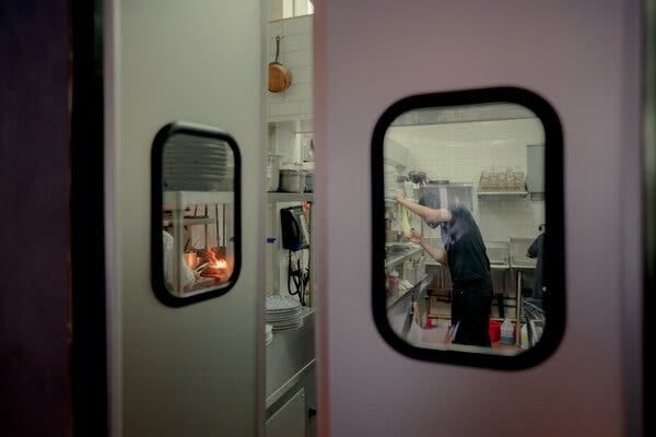 A restaurant worker seen through the window on a door leading to the kitchen.