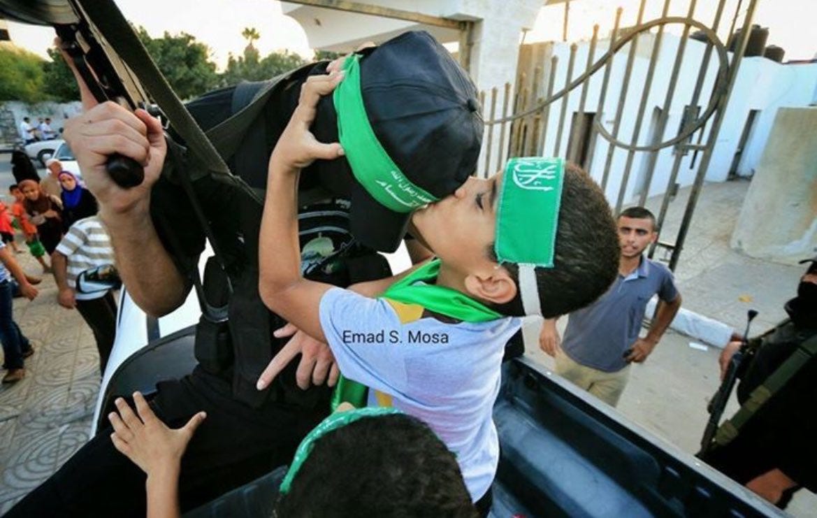 A young Palestinian child hugs and kisses a Hamas resistance fighter while standing in the bed of a pickup truck