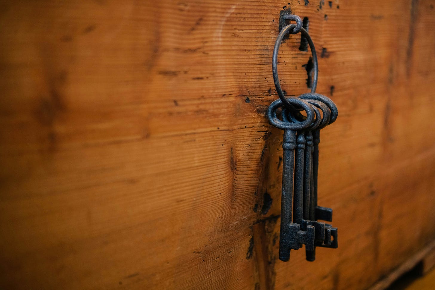 A bunch of old metal keys hangs from a ring against a brown wooden background.