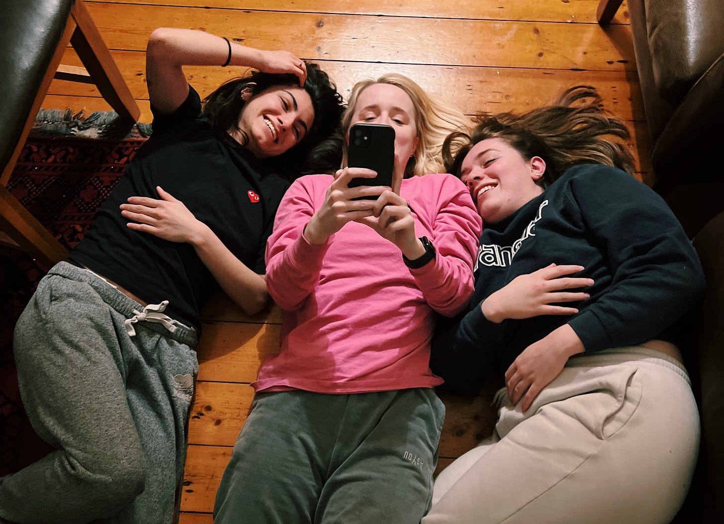 Three friends lying on a wooden floor watching TikToks on an iPhone and laughing