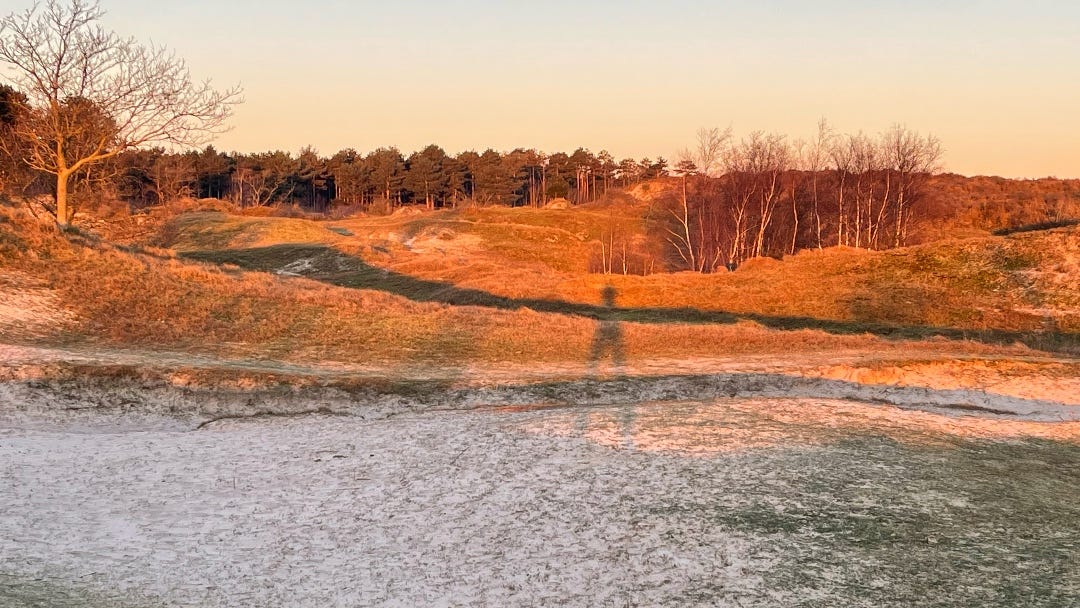 I'm standing on a dune, with the setting sun behind me. The result is a very long shadow of me, projected further on to the dunes