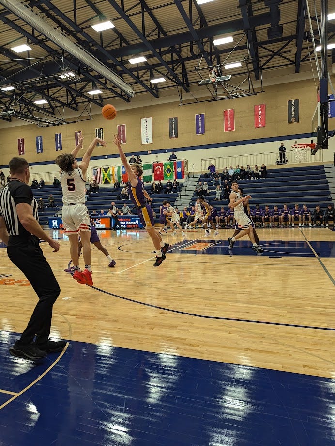 A Macalester player releases a three-point attempt over a closeout defender on the right wing. A Macalester player releases a three-point attempt over a closeout defender on the right wing.