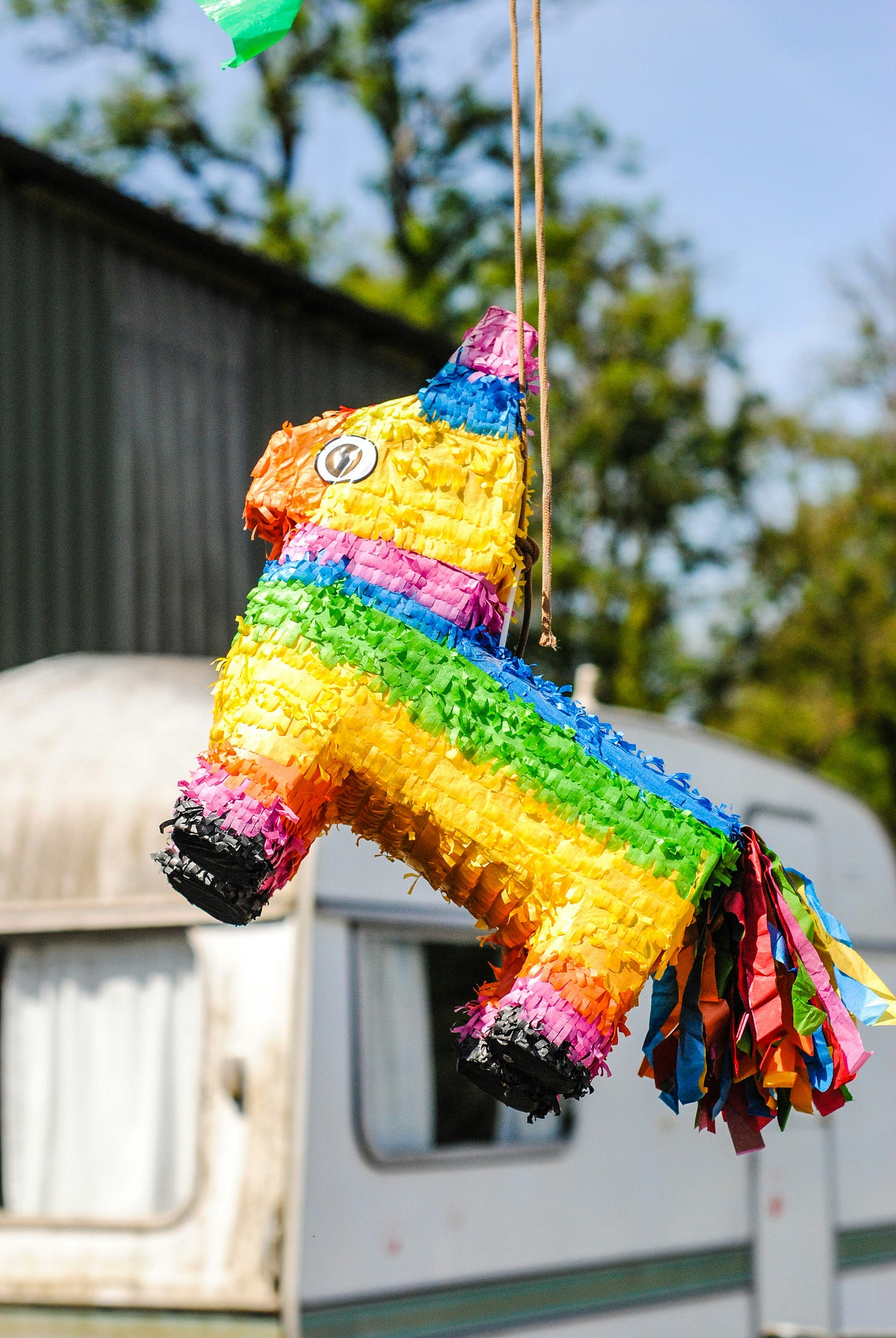 A rainbow coloured donkey pinata hangs in front of a caravan